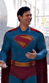 a man is wearing a superman costume and cape and smiling .