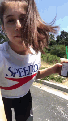 a girl wearing a speedo shirt is holding a bottle of something