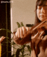 a woman is playing a violin with a plant in the background