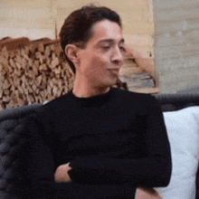 a man wearing a black shirt is sitting on a couch with his arms crossed .