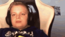 a young boy wearing headphones is sitting in a chair and making a face .