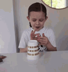 a little girl is playing with a white cup with gold stripes
