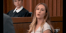 a woman is sitting in a courtroom in front of a judge and a jury .