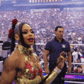 a man in a w logo shirt stands behind a woman in a gold dress