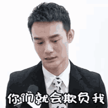 a man in a suit and tie is standing in front of a microphone with chinese writing on it .