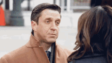 a man in a brown coat talks to a woman