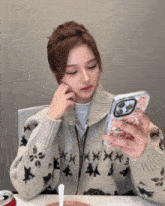 a woman in a sweater is sitting at a table looking at her cell phone