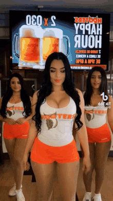 three hooters waitresses are standing in front of a tv