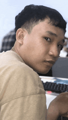 a man in a tan shirt is looking over his shoulder