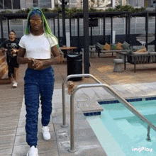 a woman with green hair is walking by a swimming pool