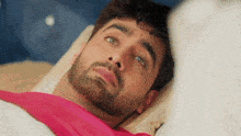 a man with a beard is laying in bed with a pink blanket on his head .
