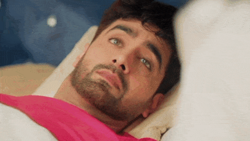 a man with a beard is laying in bed with a pink blanket on his head .