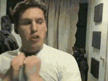 a man in a white shirt is adjusting his tie in front of a mirror
