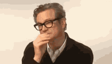 a man wearing glasses and a black jacket is covering his mouth .