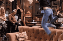 a man is jumping in the air while a group of people sit on a couch .