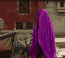 a woman wearing a black top and black pants is holding a purple scarf over her head