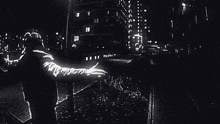 a black and white photo of a man with his arms outstretched in front of a city skyline