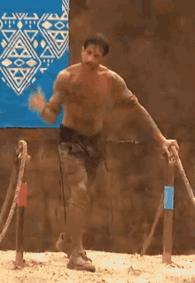 a man without a shirt is standing in front of a wooden post .