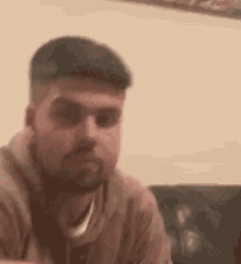 a man with a beard is sitting on a couch in a living room .