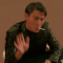 a man in a black leather jacket is smoking a cigarette and waving his hand