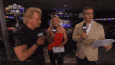 two men and a woman are standing in front of a sign that says aew