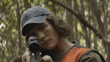 a man wearing a hat and a vest holds a rifle