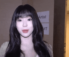 a woman with long black hair stands in front of a sign that says artist