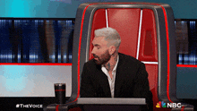 a man in a suit sits in a chair with a nbc logo on the bottom