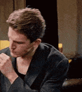 a man in a suit is sitting on a couch with his hands folded in front of him .