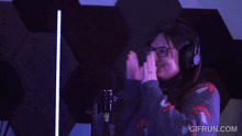 a woman wearing headphones is clapping in front of a microphone and the website gifrun.com is visible