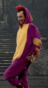 a man in a purple and yellow dragon costume stands in front of stairs