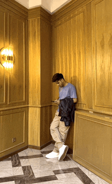 a man leaning against a wall looking at his cell phone