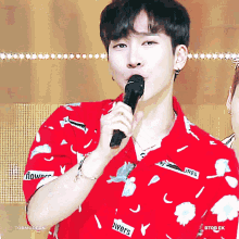 a young man wearing a red shirt with flowers on it holds a microphone