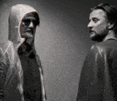 two men are standing next to each other one wearing a hooded jacket