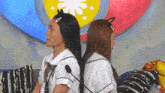 a man and a woman are sitting back to back in front of a colorful flag