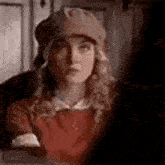 a woman wearing a hat and a red shirt is looking at the camera .