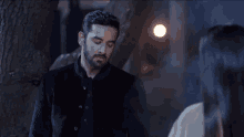 a man with a beard is standing in front of a tree looking at a woman