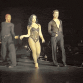 a woman in a bodysuit is walking down the runway with two men