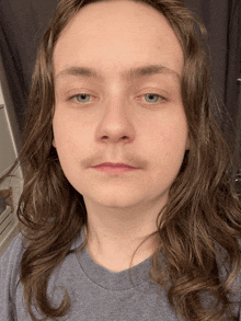 a young man with long hair and a mustache is wearing a blue shirt