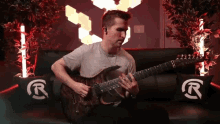 a man sits on a couch playing a guitar with a r on the pillows