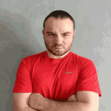 a man with a beard wearing a red t-shirt with his arms crossed .