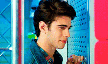 a young man in a denim jacket is standing in front of a pink wall
