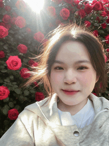 a woman stands in front of a wall of red roses