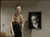 a man is standing in front of a framed picture of a man with glasses