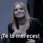 a woman in a black suit is smiling with the words te lo mereces written below her .