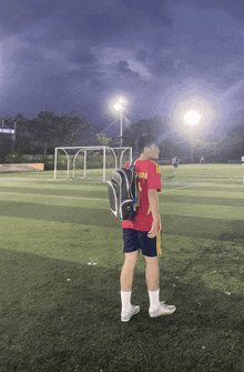 a man standing on a soccer field with a backpack and a red shirt that says v390