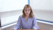 a woman in a blue polka dot shirt is sitting at a desk with a laptop .