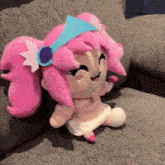 a stuffed doll with pink hair is sitting on a couch holding a lollipop .