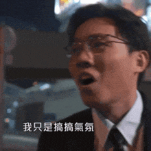 a man wearing glasses and a suit is speaking in a foreign language