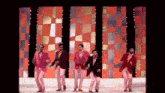 a group of men are dancing on a stage in front of a colorful background .